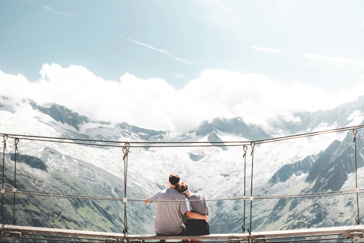 Couple sitting together on a mountain overlook with their arms around each other, facing the view ahead